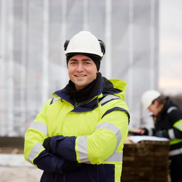 Porträttbild på en glad man i varselkläder och bygghjälm på en byggarbetsplats