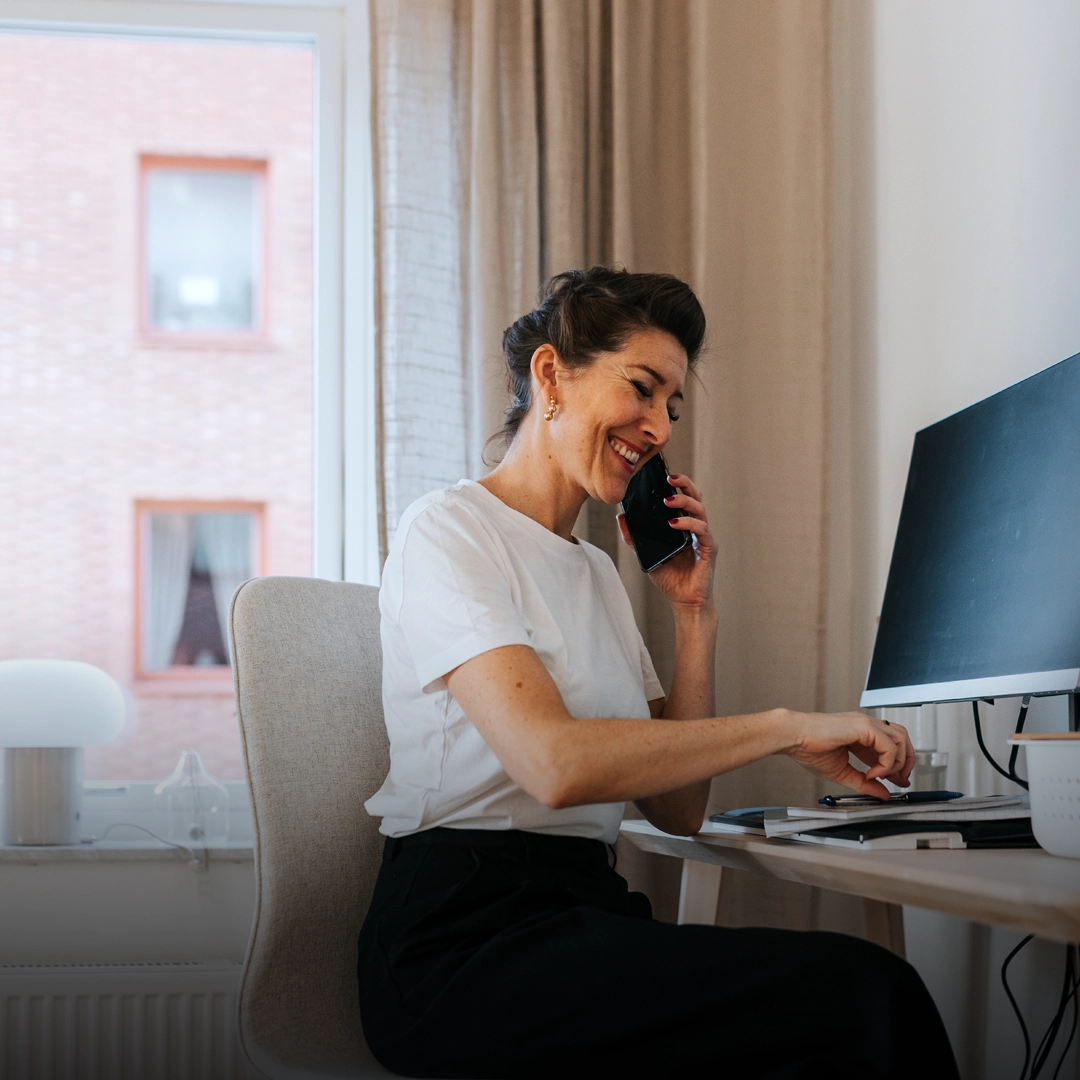 glad kvinna framför dator i kontorsmiljö pratar i telefon