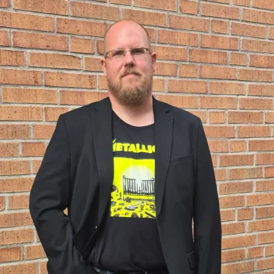 Tidigare studerande Matthias står utomhus framför en tegelvägg klädd i kavaj.