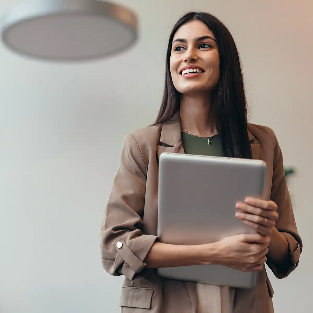 Glad kvinna som går och håller i en bärbar dator i famnen. Hon har en kavaj på sig.